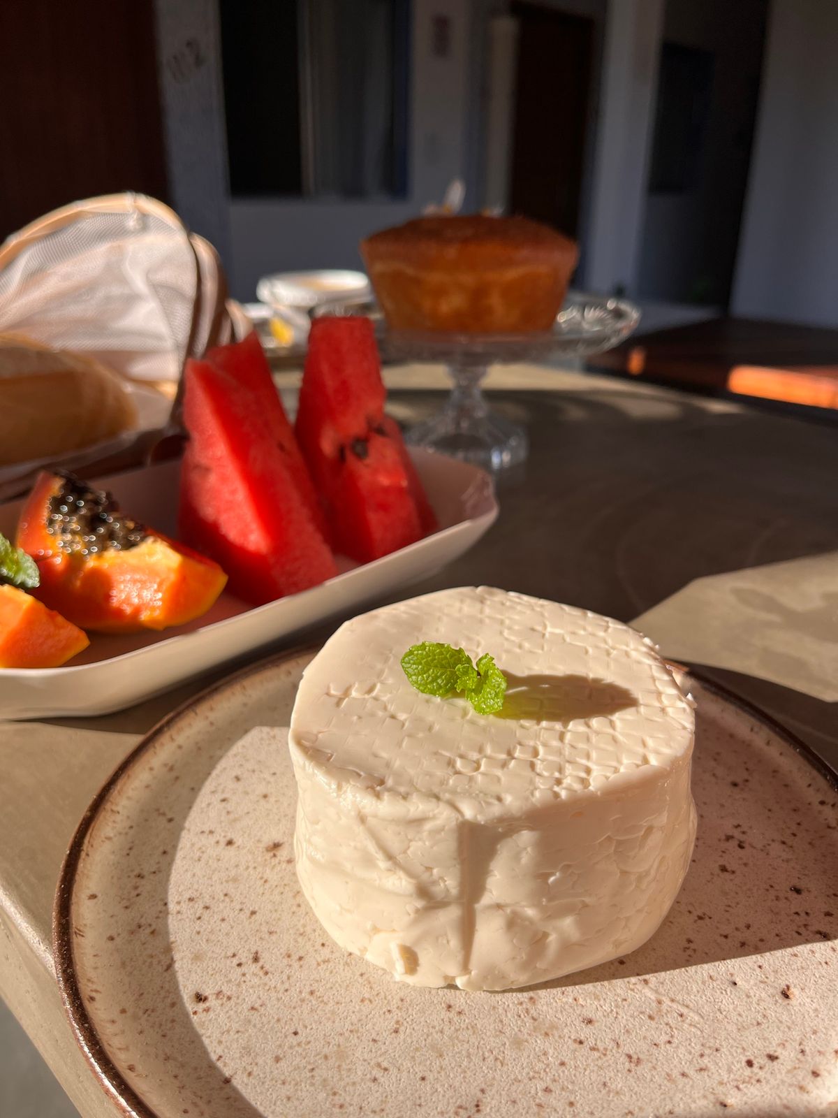 Café da manhã com queijo fresco, frutas da estação, bolo e pães, na luz da manhã