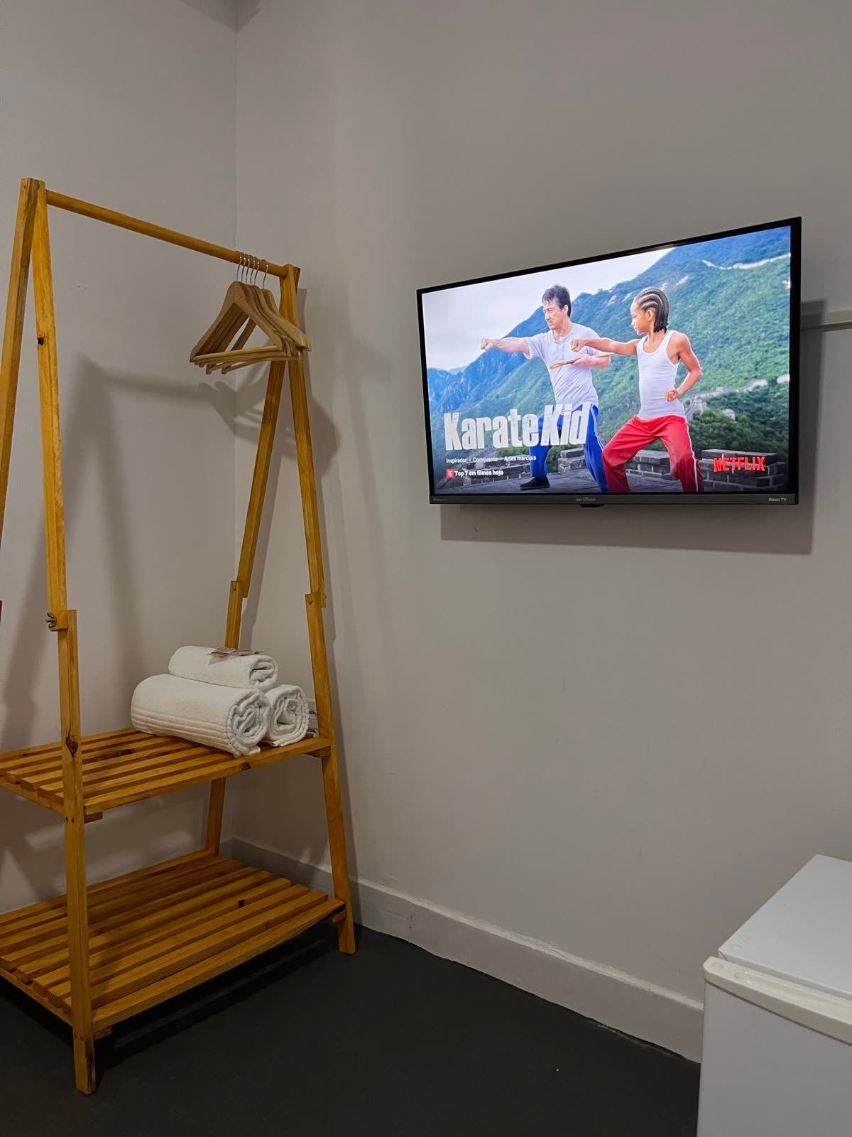 Cantinho da Suíte Concha com arara de madeira, toalhas e Smart TV