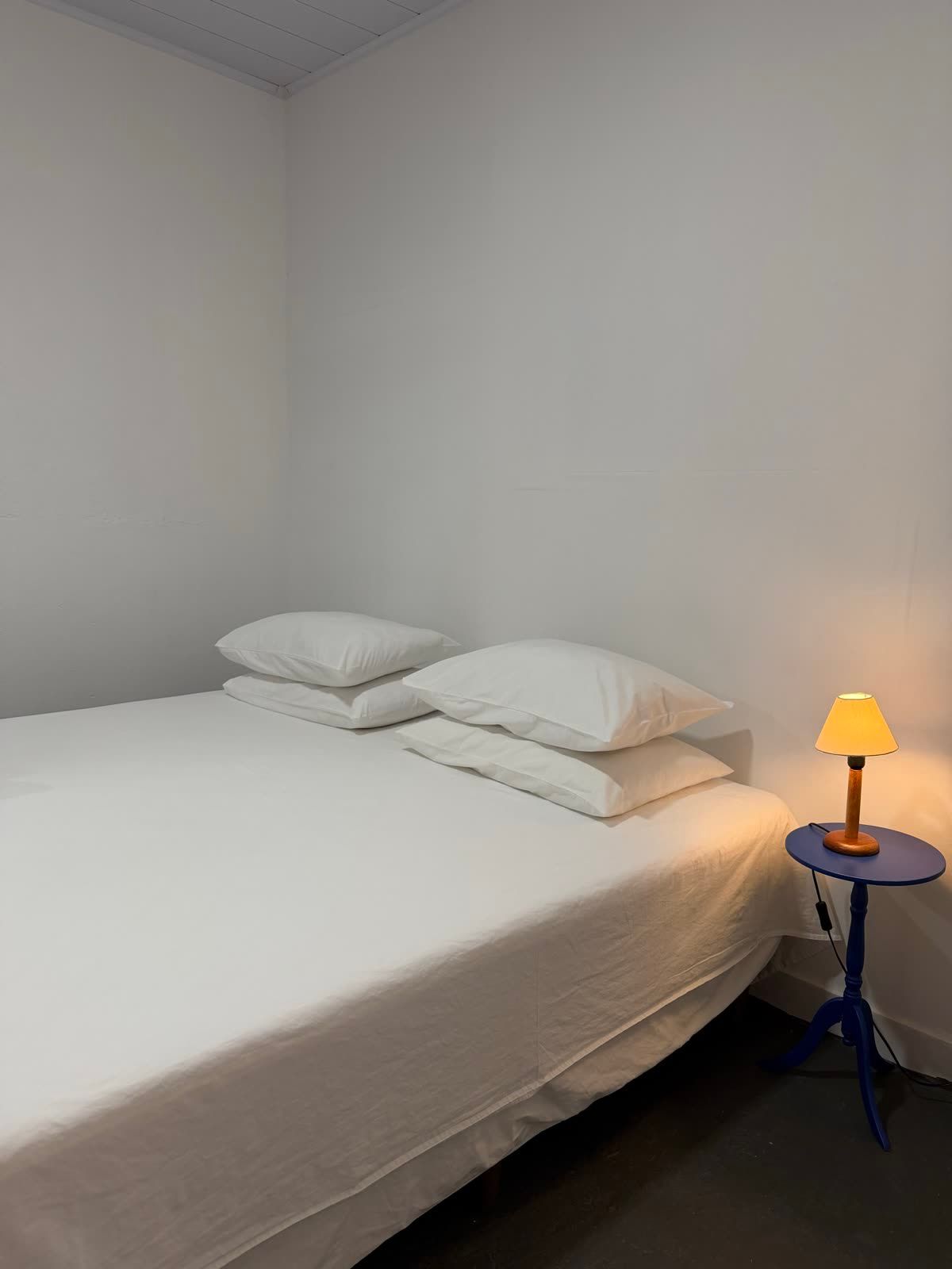 Suíte Concha: cama king arrumada com roupa de cama branca e abajur na mesa de cabeceira