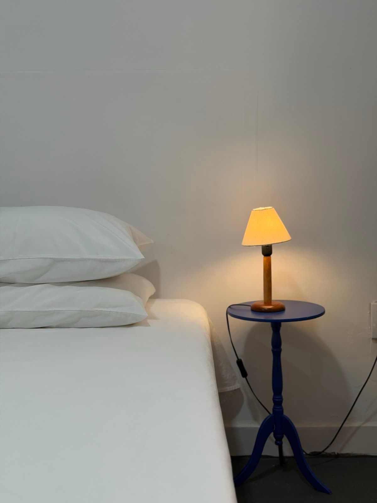 Detalhe da Suíte Concha: travesseiros e abajur de luz quente ao lado da cama