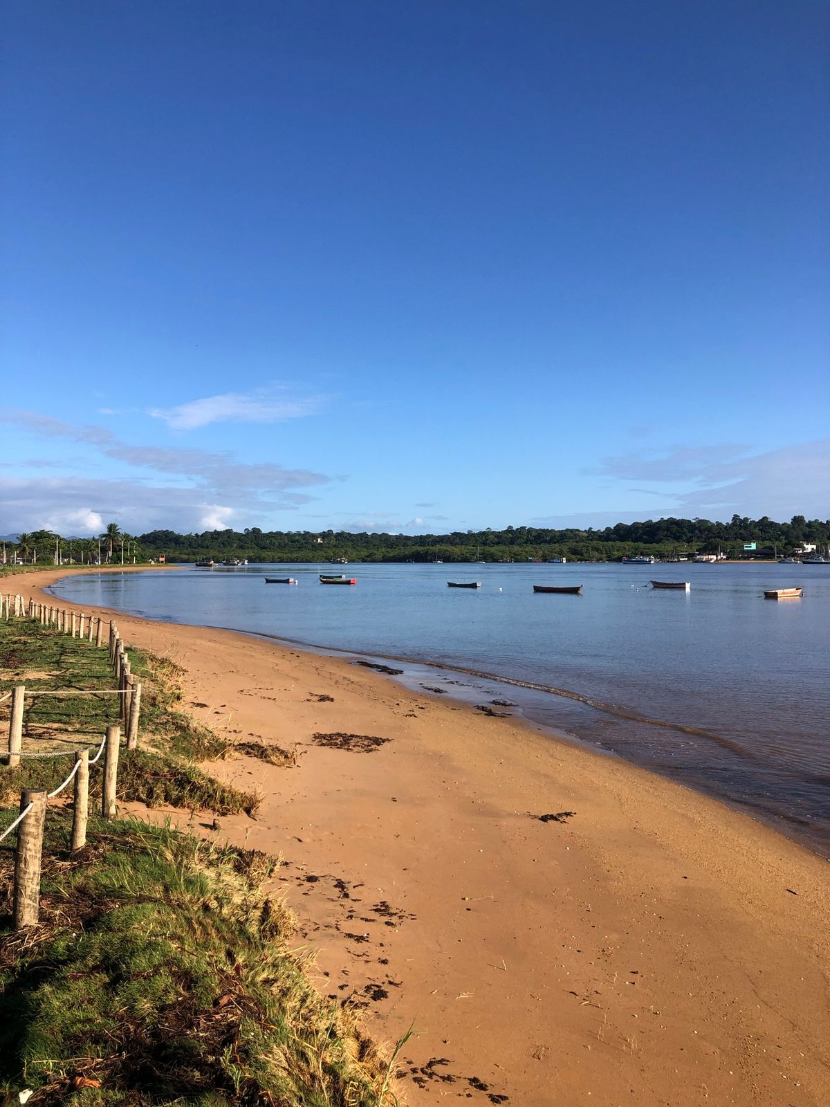 Praia de Santa Cruz com barcos ancorados e a cidade ao fundo, sob céu azul